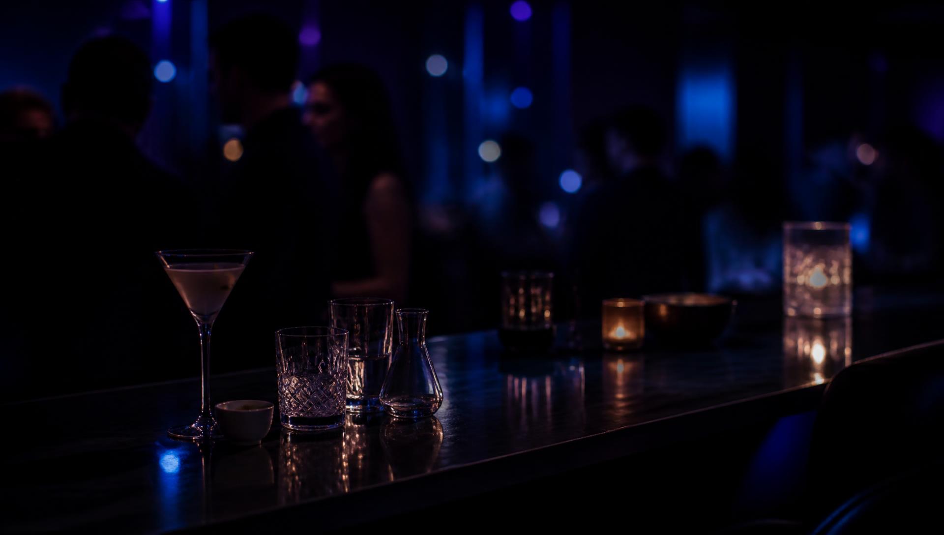 Blau beleuchtete Lounge-Bar bei Nacht mit Gläsern auf spiegelndem Tresen